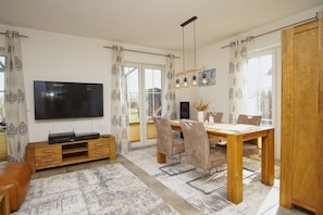 A modern living room with a flat-screen TV, wooden dining table, and comfortable seating.