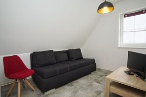 Un salon moderne avec un canapé noir, un fauteuil rouge, une table basse en bois et un téléviseur.
