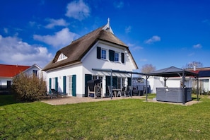Ein zweistöckiges Haus mit einem Strohdach, einer Veranda mit Gartenmöbeln und einem kleinen Schuppen.
