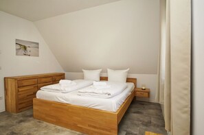 Une chambre à coucher avec un lit en bois, du linge de lit blanc, une table de chevet et une petite table de nuit.
