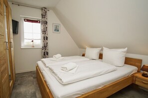 Een slaapkamer met een houten bed, witte lakens, een raam met uitzicht en een klein nachtkastje met een lamp.