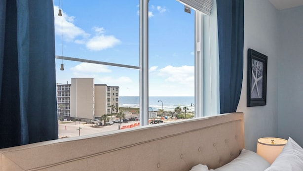Une chambre d’hôtel dotée d’une grande fenêtre donnant sur la plage et les bâtiments environnants.