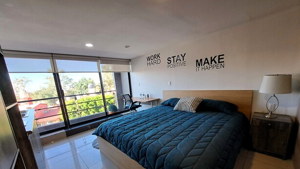 A modern bedroom with a large bed, a nightstand, a desk, and a view through large windows. - S10 PREMIUM SUITE Full Service WiFi (Atizapan de Zaragoza)