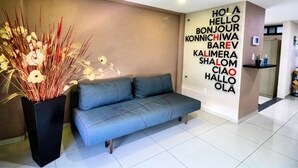 A modern hotel lobby with a grey sofa, a decorative plant, and a wall with multilingual greetings. - S10 PREMIUM SUITE Full Service WiFi (Atizapan de Zaragoza)