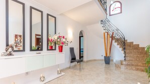 A spacious foyer with a marble floor, a white console table with decorative items, a black chair, and a staircase with a wrought iron railing.