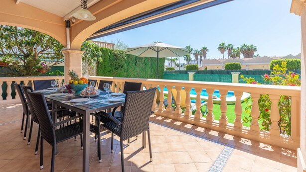 An outdoor patio with a table set for dining, surrounded by chairs, and overlooking a pool area.
