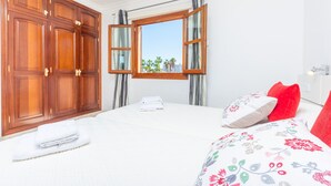 A bedroom with a large wooden wardrobe, a bed with floral bedding, and a window with curtains.