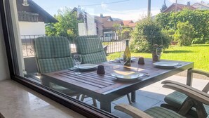 A dining area with a table set for two, chairs, and a view of a garden and houses. - Auszeit by Interhome (Oy-Mittelberg)