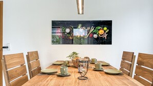A wooden dining table with six chairs, a glass vase with a plant, and a framed artwork above the table. - Auszeit by Interhome (Oy-Mittelberg)
