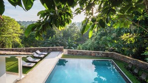 A rectangular swimming pool with a stone border, surrounded by a stone wall and a white pergola. - Villa Poojakanda (Koggala)