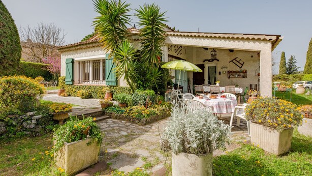 Un bâtiment de style rustique doté d’un patio aménagé avec des espaces de détente en plein air et d’un jardin où poussent diverses plantes et fleurs.