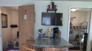 A compact kitchen with a wooden island, two bar stools, a flat-screen TV, and a coffee maker. - Norfork Lake - Quaint 2 bedroom, no stairs. By the pool -camp store - pavilion. (Elizabeth)