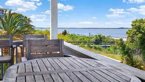 A wooden deck with a table and chairs, overlooking a body of water and greenery. - Cozy Beach and Racquet Condo | Heated Pool Access (Tybee Island)