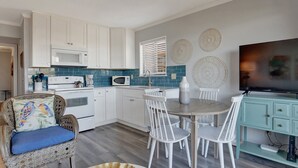 A modern kitchen with white cabinets, a dining table with white chairs, and a teal-colored cabinet. - Cozy Beach and Racquet Condo | Heated Pool Access (Tybee Island)