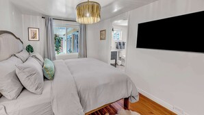 Ett sovrum med en säng, ett stort fönster, en taklampa och en tv som är monterad på väggen.