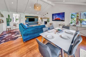En moderne stue med en blå sofa, et spisebord dækket til fire personer, og et stort fladskærms-tv monteret på væggen.
