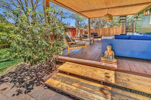 En udendørs terrasse med træmøbler, en Buddha-figur og et overdækket siddeområde.