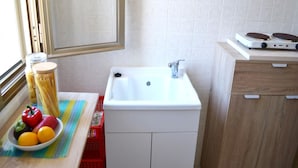 A small kitchen with a white sink, a stove, and a window. There is a bowl of fruit on the counter. - Kitai Air-conditioned Studio Holiday Home in San Foca (Melendugno)