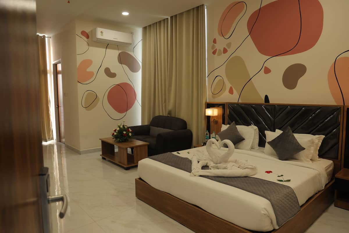 Une chambre d’hôtel moderne avec un grand lit, un canapé, une petite table ornée d’un vase de fleurs et des œuvres d’art abstraites accrochées au mur.