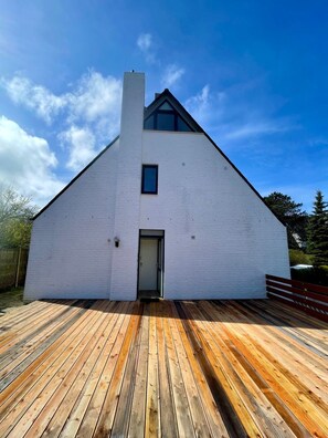 A modern white building with a sloped roof and a wooden deck in front.
