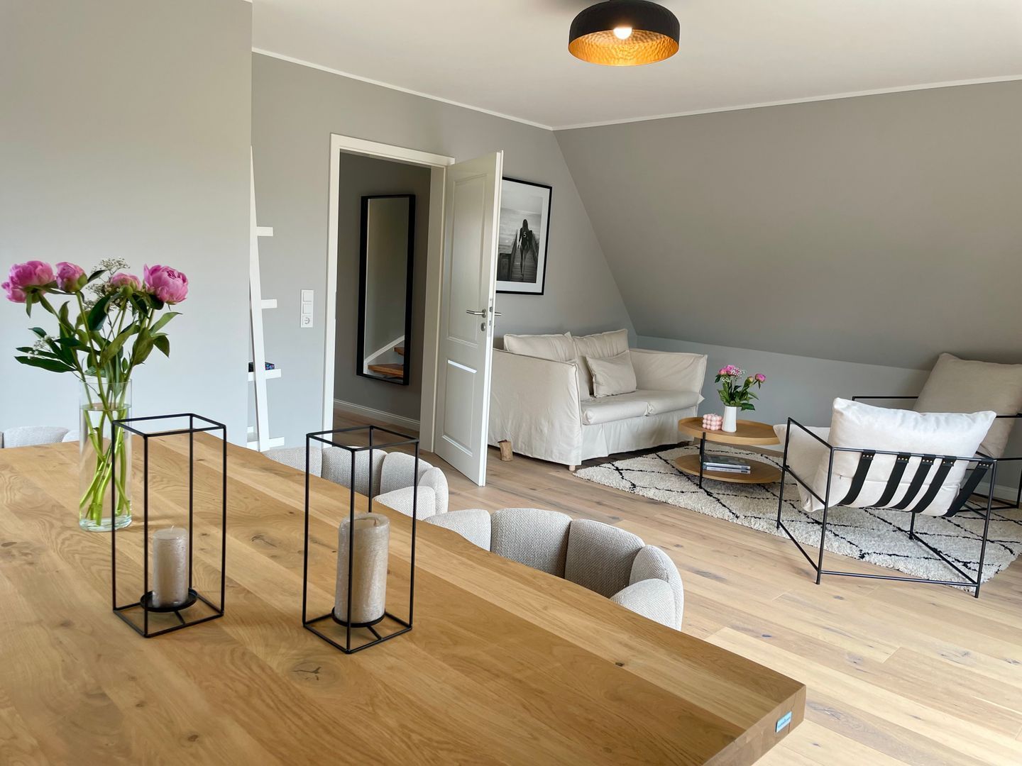 A modern living room with a wooden dining table, white sofas, and a black and white striped armchair.