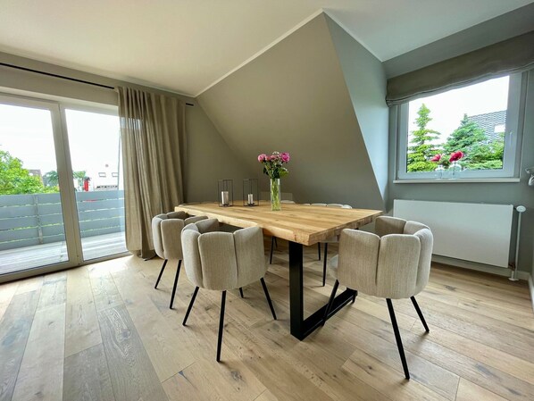 Un comedor moderno con una mesa de madera y seis sillas, un jarrón con flores y vistas al exterior.