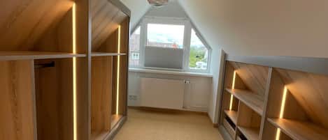 Ein schmaler Korridor mit Holzverkleidung, eingebauten Regalen und einer geneigten Decke.