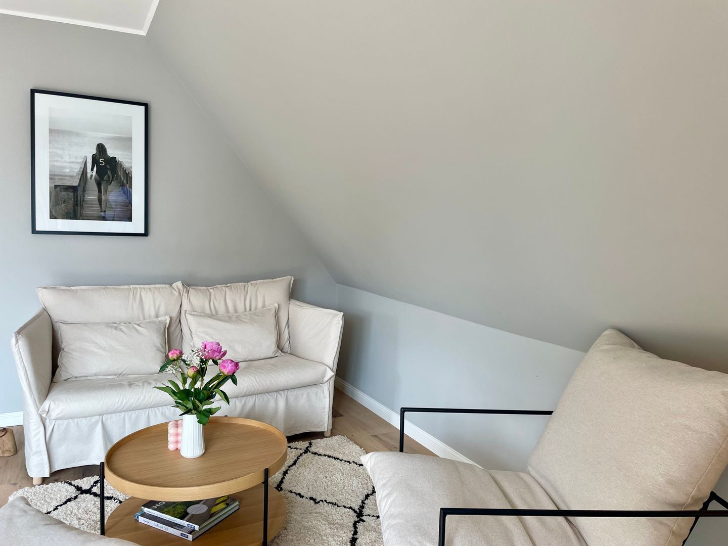 A living room with a beige sofa, a wooden coffee table with a vase of flowers, and a framed picture on the wall.