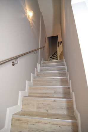 A wooden staircase with white trim, a handrail, and a wall-mounted light fixture.