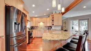 Eine moderne Küche mit einem Edelstahlkühlschrank, Holzschränken, Granitarbeitsplatten und einer Bar mit Sitzgelegenheiten.