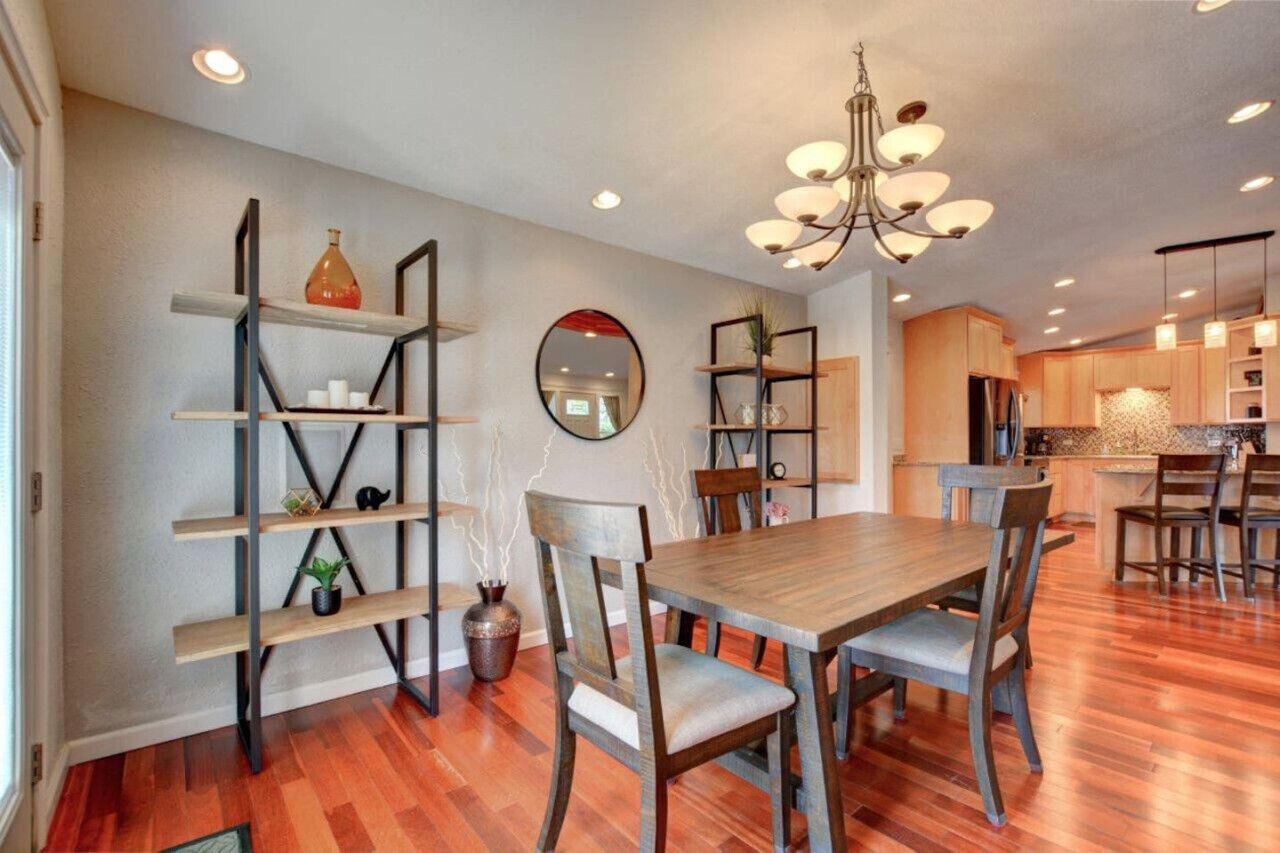 Un espace repas moderne avec une table et des chaises en bois, un lustre et des étagères intégrées ornées d’objets décoratifs.