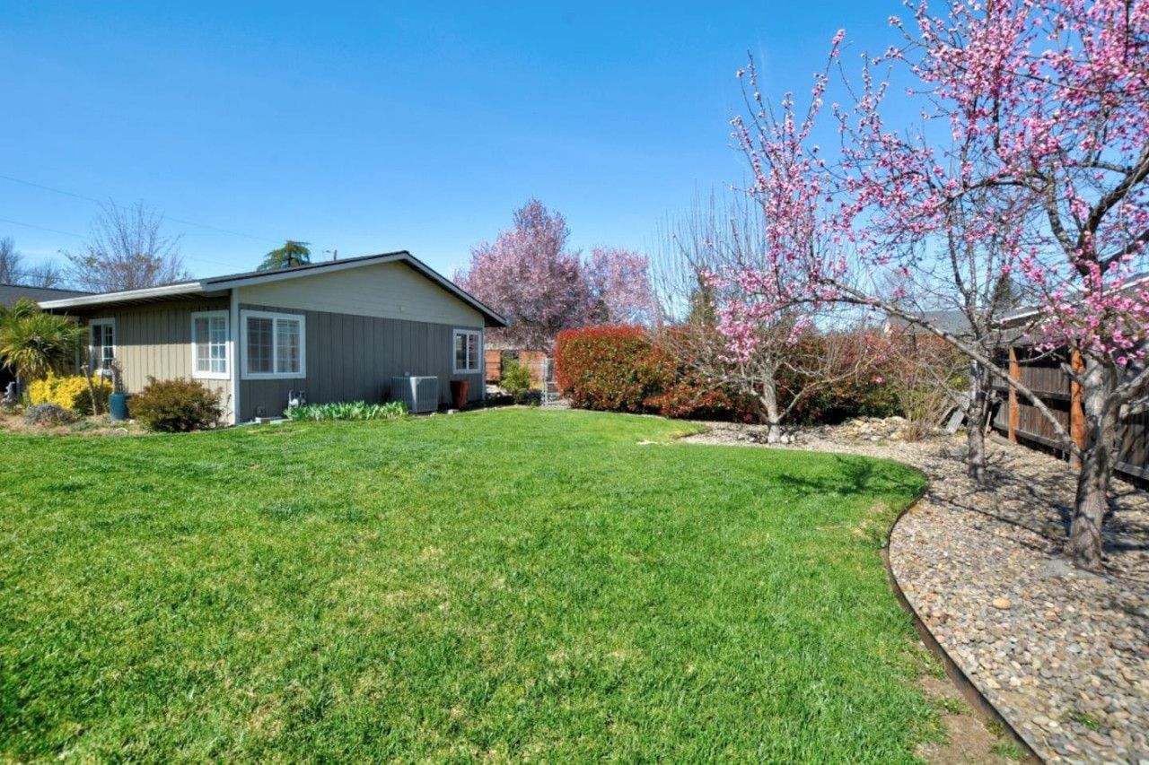 A residential property with a well-maintained lawn, a wooden deck, and a variety of flowering trees.