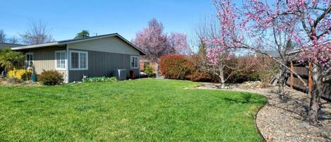 A residential property with a well-maintained lawn, a wooden deck, and a variety of flowering trees.