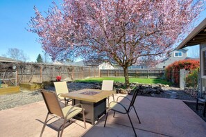 A patio with a table and chairs, a tree with pink blossoms, and a fenced backyard.