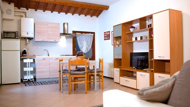 Cocina compacta con microondas, estufa y lavamanos.  Hay una zona de comedor con mesa y sillas. Un televisor está montado en un mueble de madera.