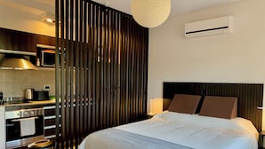 Ein modernes Hotelzimmer mit einem großen Bett, einer Küchenzeile, einer vertikalen Holzwand und einer Klimaanlage an der Wand.