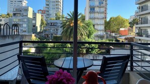Ein Balkon mit Tisch und Stühlen, der auf einen Stadtblick mit verschiedenen Gebäuden und Grünflächen blickt.