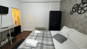 A bedroom with a bed, a desk, a wardrobe, and a wall-mounted TV. - Studio Apartment Sleeps 2 with Ensuite (London)