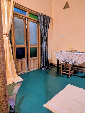 Une piĂšce avec une porte en bois, une table recouverte dâune nappe Ă motifs floraux et un tabouret.