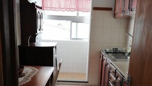 Una cocina con una mesa de comedor, sillas, armarios y una ventana con cortina a cuadros.