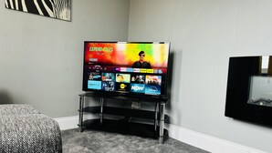 A television on a stand in a room with a carpeted floor and a framed picture on the wall.