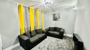 A living room with a grey carpet, two dark sofas, a wall-mounted TV, and a zebra-patterned artwork.