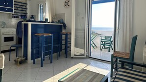 A kitchen with blue bar stools, a white stove, and a view of the sea through a sliding glass door. - Blue orison house Tinos for 5 persons with seaview (Tinos Regional Unit)