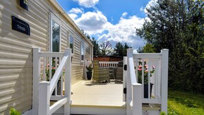 Uma casa móvel com deck de madeira, corrimãos brancos e uma placa com o nome 'Triesle'.