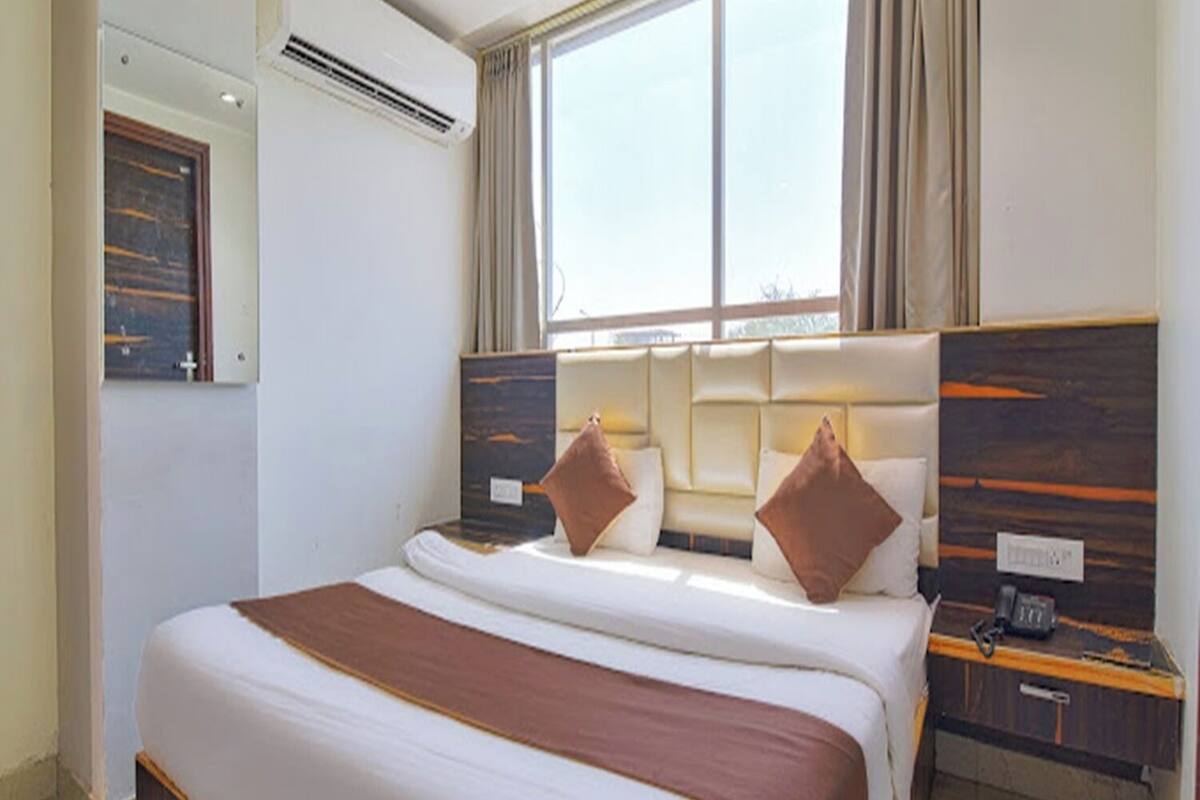 Une chambre d’hôtel avec un grand lit, une table de chevet, une commode, un miroir et une fenêtre avec des rideaux.