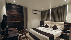 A modern hotel room with a large bed, a desk, a chair, and a wardrobe.