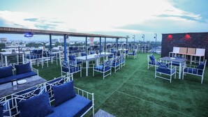 A rooftop bar with outdoor seating, a covered area, and a view of the cityscape.