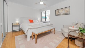 A bedroom with a bed, bedside table, bench, chair, and a ceiling fan.
