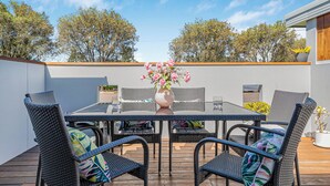 An outdoor patio with a table and chairs, a vase with flowers, and a view of trees.