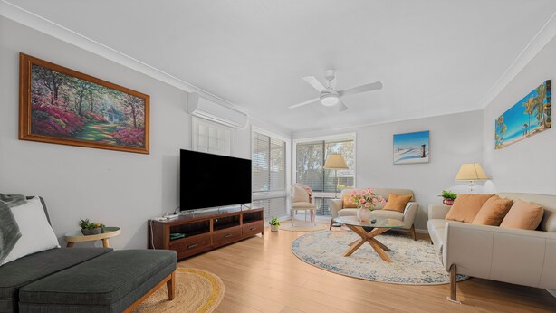A modern living room with a flat-screen TV, a sofa, a coffee table, and a ceiling fan.